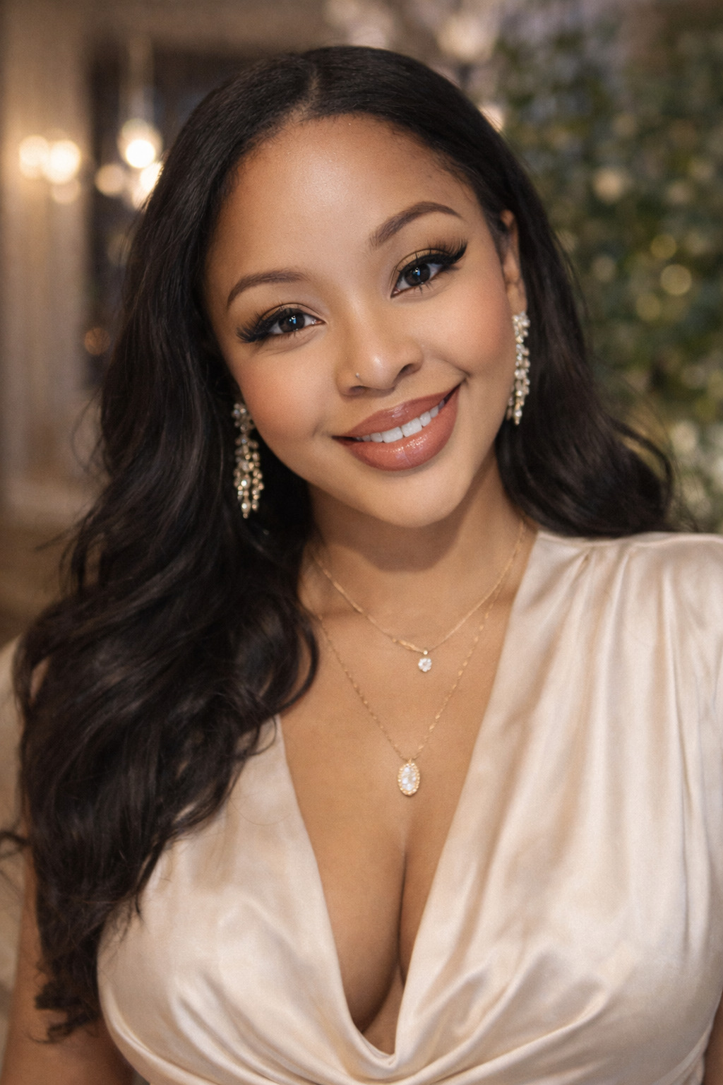 Portrait of Kenise Taylor wearing an elegant cream dress and statement earrings, smiling in a softly lit indoor setting.