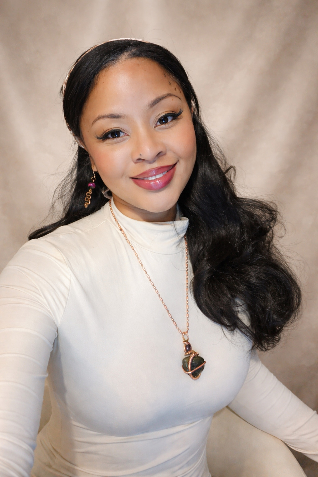 Portrait of Kenise Taylor smiling indoors, wearing a cream top and gemstone necklace against a neutral backdrop.